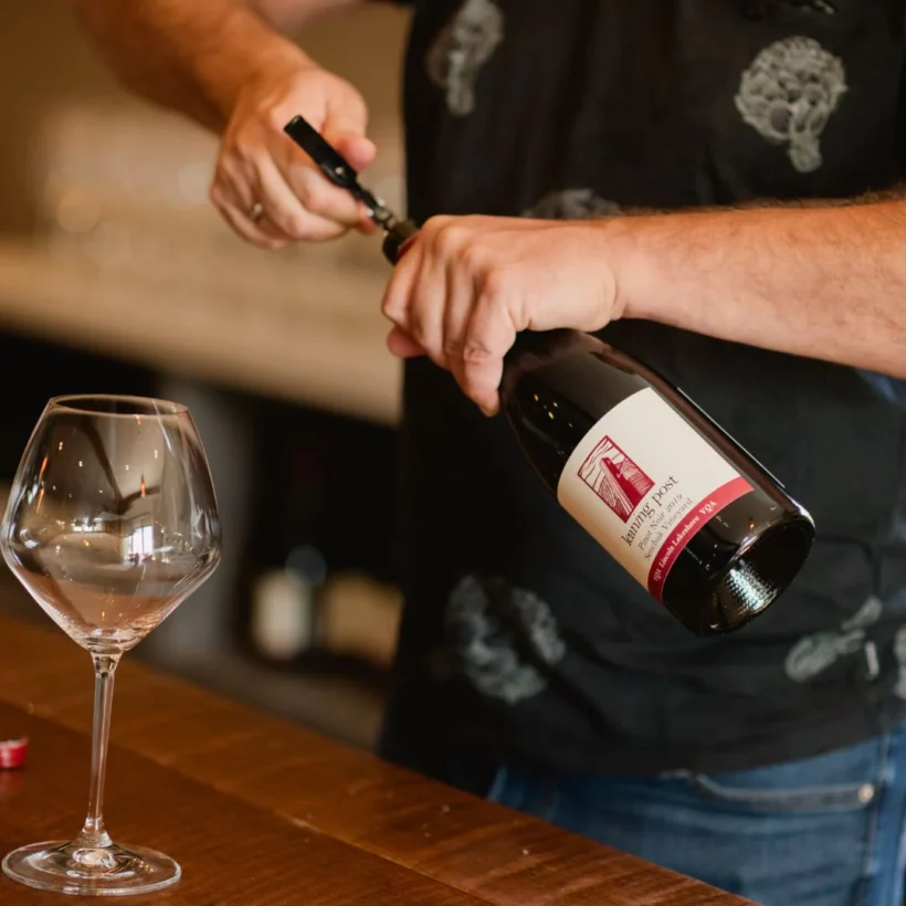 A person uncorking Leaning Post Winery’s red wine